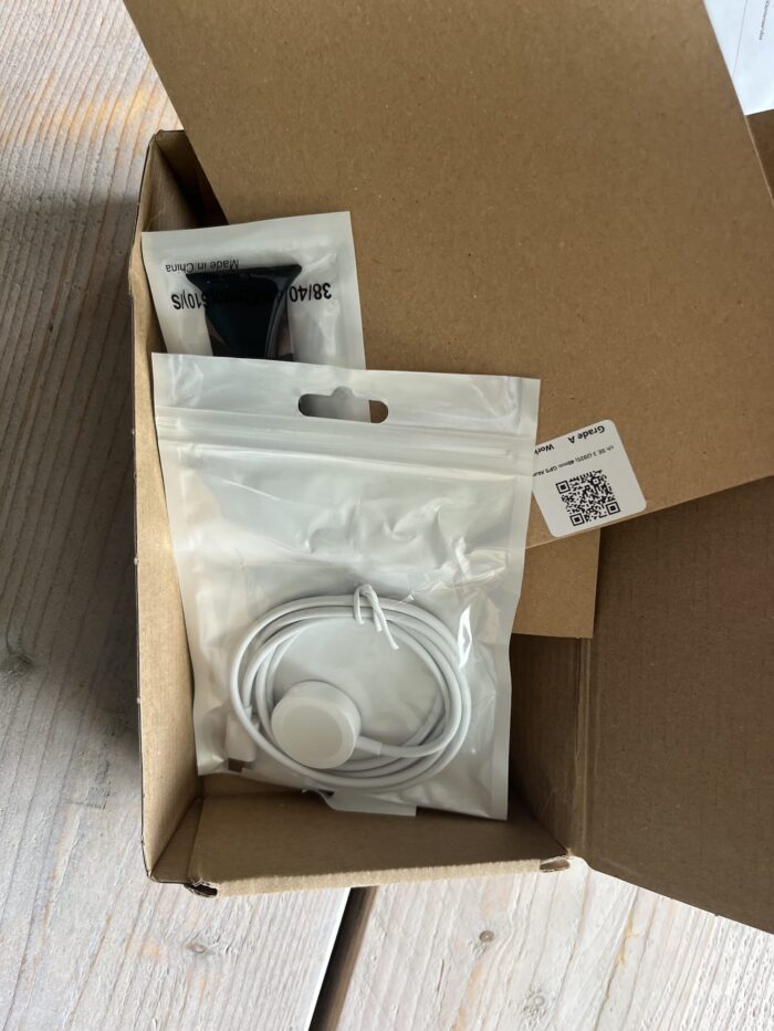 Inhoud van het Back Market pakket: Apple Watch SE met magnetische oplader en horlogebandje in plastic zakjes